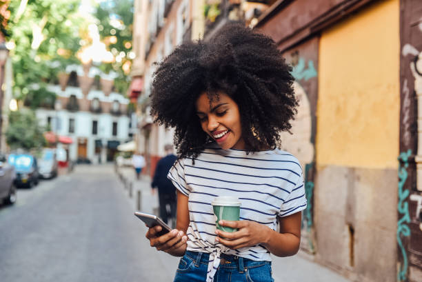 istock Beautiful Afro girl using phone and drinking coffee on the move 1251346267
