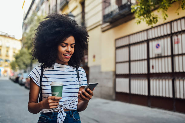 istock Cute girl enjoying coffee and using phone while walking through the city 1251346276