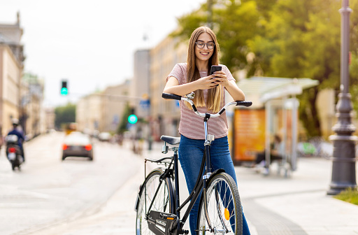 Attractive young woman using smartphone while out cycling through the city