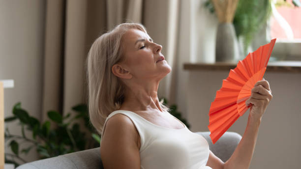 sudorosa señora mayor usando papel agitando ventilador. - menopausia fotos fotografías e imágenes de stock
