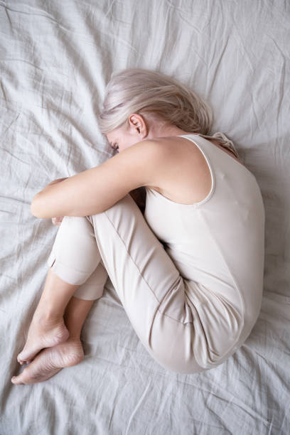 istock Stressed middle aged woman lying on bed in fetal position. 1251350012