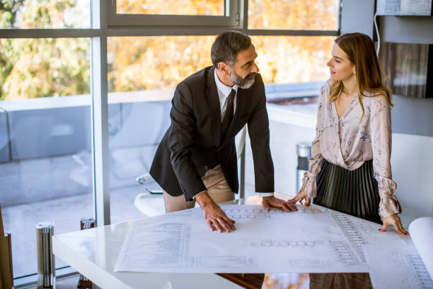 istock Handsome architect and his young female colleague checking plans and blueprints 1251353523