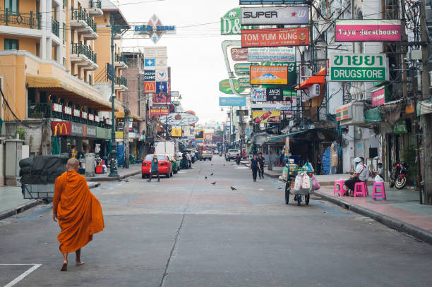 Buddhist monk walks barefoot down Khao San Road Bangkok BANGKOK, THAILAND - 29. MAY 2018. An unknown Buddhist monk walks barefoot down the city street. Khao San Road is popular tourists street in Bangkok Thailand. Day editorial shot khao san road stock pictures, royalty-free photos & images