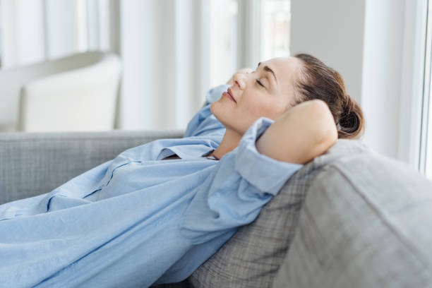 Exhausted young woman relaxing on a sofa Exhausted young woman relaxing on a sofa lying back with her hands behind her head and closed eyes with a quiet smile of pleasure napping stock pictures, royalty-free photos & images