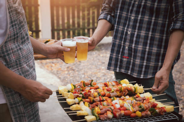 junge männer jubeln für einen drink auf einer grillparty unter freunden. essen, trinken, menschen und familienzeitkonzept. - barbecue chicken fotos stock-fotos und bilder