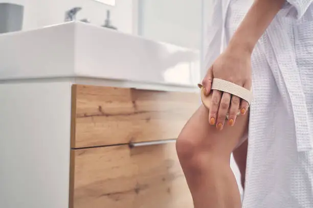 Close up of young woman hand massaging leg with lymphatic detox massage brush