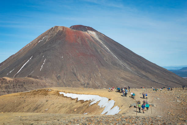 Tourists walking on the Tongariro Alpine Crossing with Mount Ngauruhoe in the background, Tongariro National Park, New Zealand Tourists walking on the Tongariro Alpine Crossing with Mount Ngauruhoe in the background, Tongariro National Park, New Zealand tongariro national park photos stock pictures, royalty-free photos & images