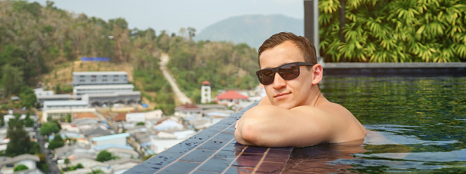 handsome stylish man in sunglasses rests on outdoor swimming pool closeup