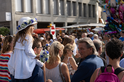 Little girl with straw hat sitting on shoulder is watching the parade of schoolkids and a man is looking back on Rutenzug on the 4th of july at Jugendfest Brugg 2019.