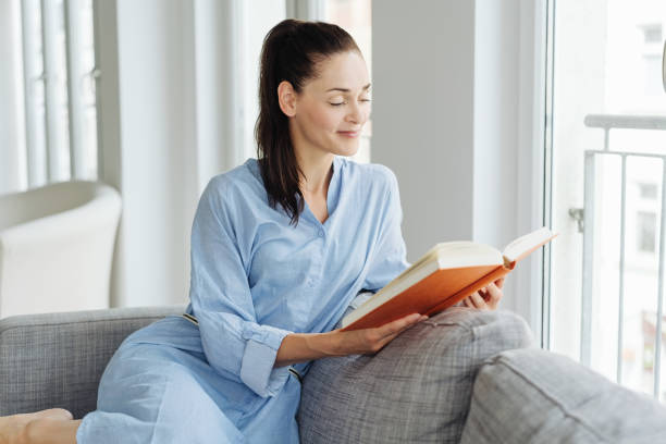 istock Young woman reading a book, sitting on the couch 1251362623