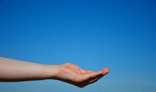 a woman's hand against the blue sky. the palm of the hand is folded, as if asking for something