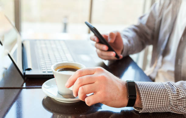 istock Man in smart watch drinking coffee on work space. Man using laptop, holding smart phone for business work or study. Close up smart watch on male hand. Freelancer works in cafe, office, texting massage 1251364748