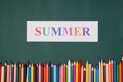 Summer vacation concept. Top above overhead view photo of summer paper and colorful crayons isolated on greenboard