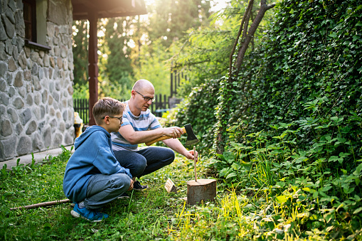 Father is explaining son how to chop wood safely with axe. \nNikon D850