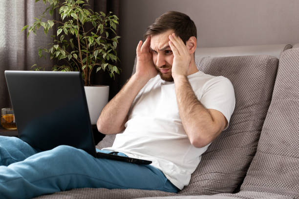istock Stress caucasian gloomy man in stress working from home office wearing protective mask using laptop and internet. Remote work, freelancer home office workplace on sofa. Coronavirus covid 19 quarantine 1251367943