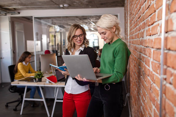 Let's go over the details Two female colleagues working together on the laptop while standing travel agency stock pictures, royalty-free photos & images