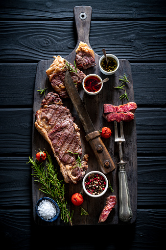 Carved Strip Steak Top Loin steak beef meat with carver fork on chopping board over black wood background