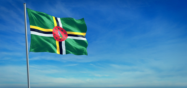 The National flag of Dominica blowing in the wind in front of a clear blue sky