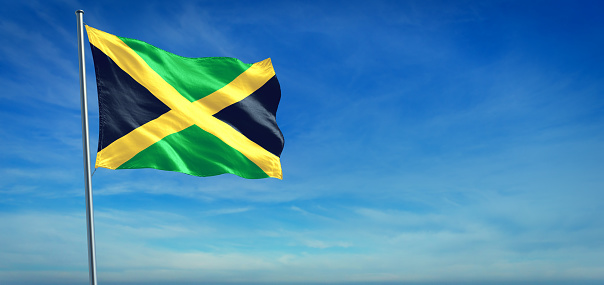 The National flag of Jamaica blowing in the wind in front of a clear blue sky