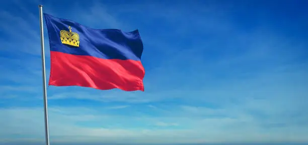 The National flag of Liechtenstein blowing in the wind in front of a clear blue sky