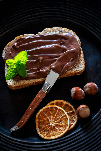 istock Chocolate cream spread on bread slice and hazelnuts on a dark black plate 1251376582