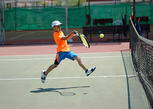 a boy is playing tennis on the hardcourt with forehand