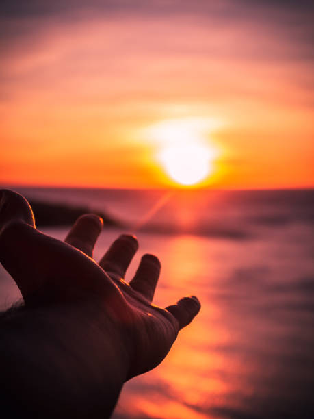 istock A hand reaching out to a setting sun with the light rays hitting the hand at a seaside 1251383937