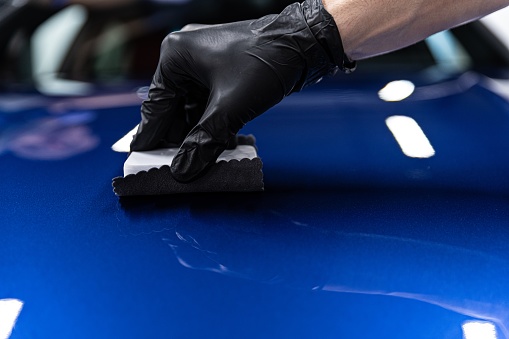 Man worker of car detailing studio applying ceramic coating on car paint with sponge applicator. Car detailing