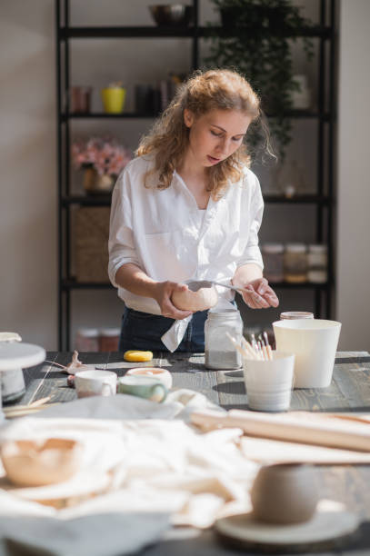 istock Female potter glazing raw unburned ceramic cup using brush. Earthenware mug putting colorant on pottery workshop 1251392087