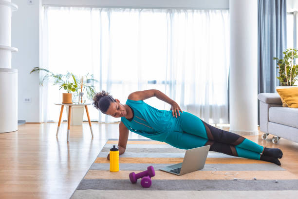 Multitasking is the easiest thing I've ever done Beautiful woman doing fitness exercise at home while looking at laptop. pilates photos stock pictures, royalty-free photos & images