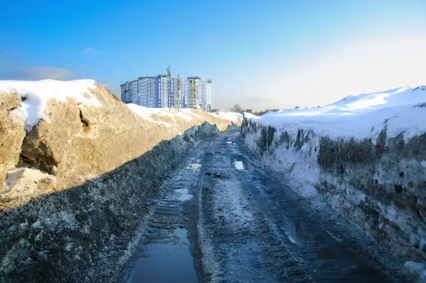Spring landscape with snowdrifts and puddles on the road in the north. The construction of a multi-storey residential building.