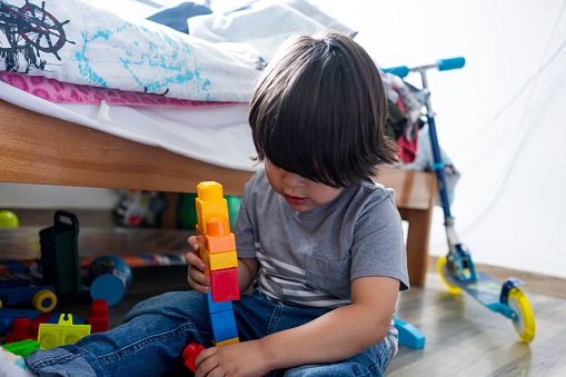 Latino boy from Bogota Colombia between 2 and 4 years old playing on the floor of his room with blocks and other toys during the quarantine by Covid 19