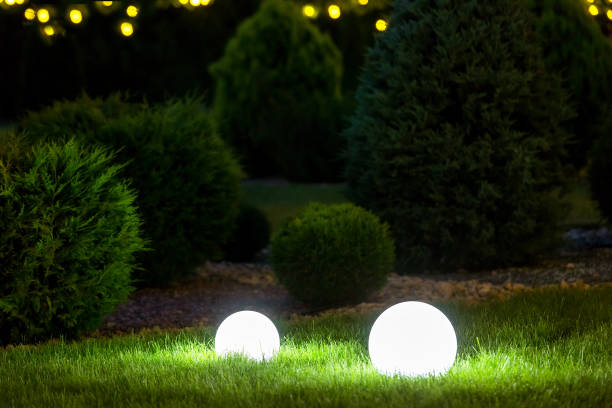 istock backyard ground 2 light garden with lantern electric lamp with sphere diffuser in green grass with thuja bushes and stone mulching in park with landscaping, closeup night scene nobody. 1251400794