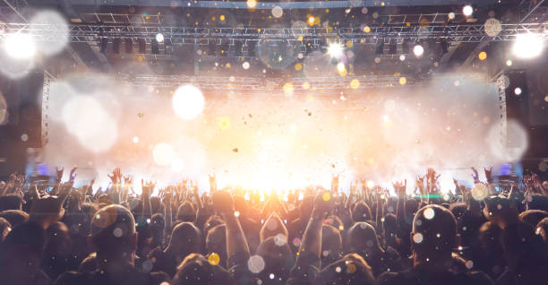 Concert stage, people are visible waving and clapping, silhouettes are visible A shot taken in front of a concert stage lit in the night, people are visible waving and clapping, but no one is recognizable. popular music concert stock pictures, royalty-free photos & images