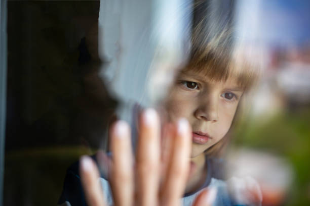 istock Sad little boy behind window glass 1251405295