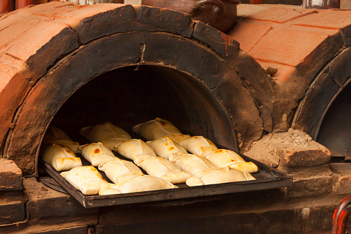 Chilean fresh EMPANADAS DE PINO, a kind of flat cake or meat pie made of pastry filled with meat, egg and olives, cooking in a mud greda handmade rustic oven in the Chilean National Independence day 18 september. Regional food from Chile. Baking concept. Chilean independence day concept.