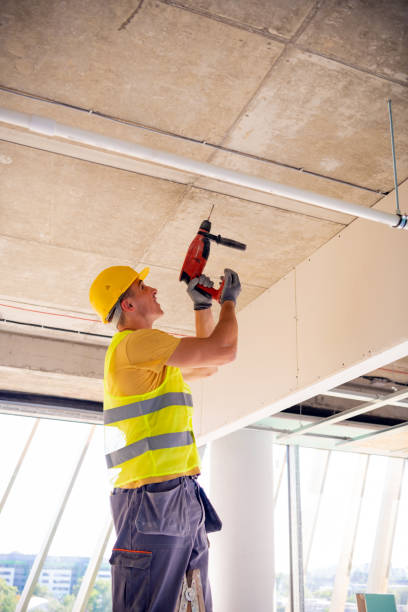 istock Young male construction worker in yellow hardhat drilling the wall with electric drill tool. Close-up front portrait with copy space 1251409161