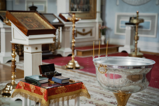 Orthodox church. Candles, cross, icon, prayer book, candles and Bible on table, baptismal font. Preparing for baptism of newborn child in Holy water. Sacrament of baptism