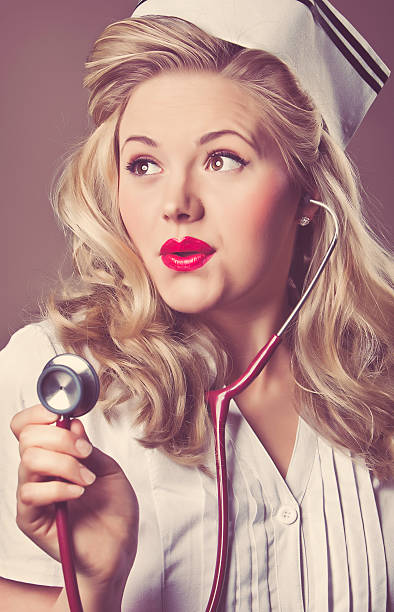 Retro Nurse Portrait of a young retro nurse holding up her stethoscope looking away from the camera with a cute look on her face.. 40s pin up girls stock pictures, royalty-free photos & images