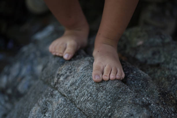 A closeup of a little boys bare feet that is balancing on the edge of a rough rock to convey a dangerous situation. stock photo