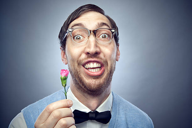 Nerd Student Giving Flower Nerdy IT young man wearing a bow tie, blue sweater vest, and horn rimmed glasses makes a happy, goofy face while offering a flower to someone he loves.  Horizontal on gray / blue background with copy space. horn rimmed glasses stock pictures, royalty-free photos & images