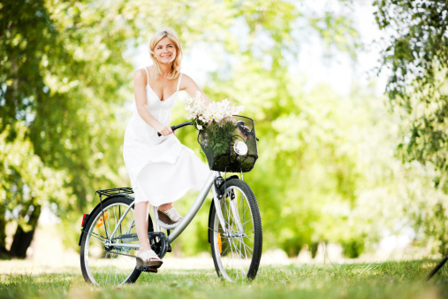 Beautiful young blonde woman is riding a bike. She is surrounded by lush greenery.   