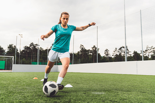 Young female soccer player training on a football field. Young woman practicing her skills, trying to become a professional athlete.