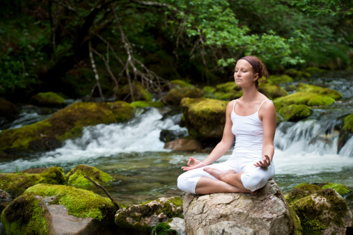 Woman meditating in easy pose while sitting on rock