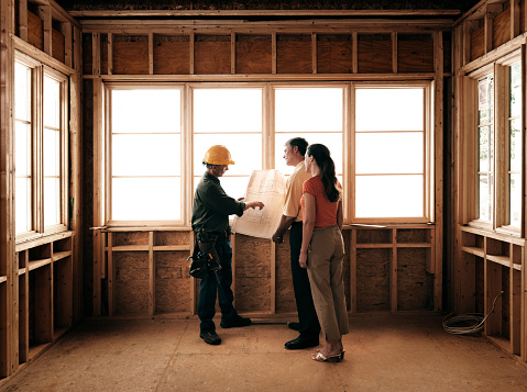 Husband and wife consulting with a architect inside a home under construction.