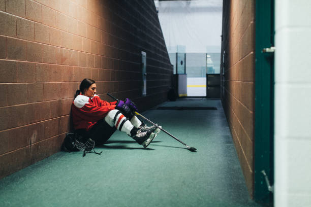 Women's Ice Hockey Player Portrait A female hockey player gets sits in the corridor after a tough loss on the ice. Image taken in Utah, USA. woman defeat stock pictures, royalty-free photos & images