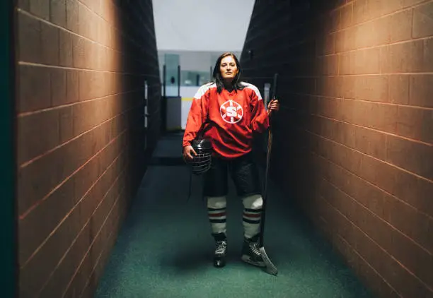 Portrait of a women's ice hockey offense player before a recreation league hockey game. She is standing in a corridor ready to play the game. Image taken in Utah, USA.