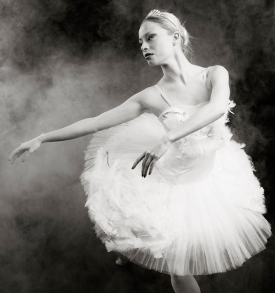 Young ballerina dancing on black foggy background.Black and white image.