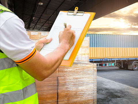 Cargo freight industry warehouse shipment and transportation. Worker courier holding clipboard inspecting checklist load cargo into a truck.