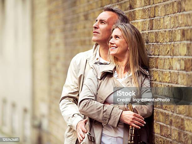 Uśmiechnięta Dojrzałych Para Obejmując I Stojących Obok Mur Z Cegły - zdjęcia stockowe i więcej obrazów 50-59 lat
